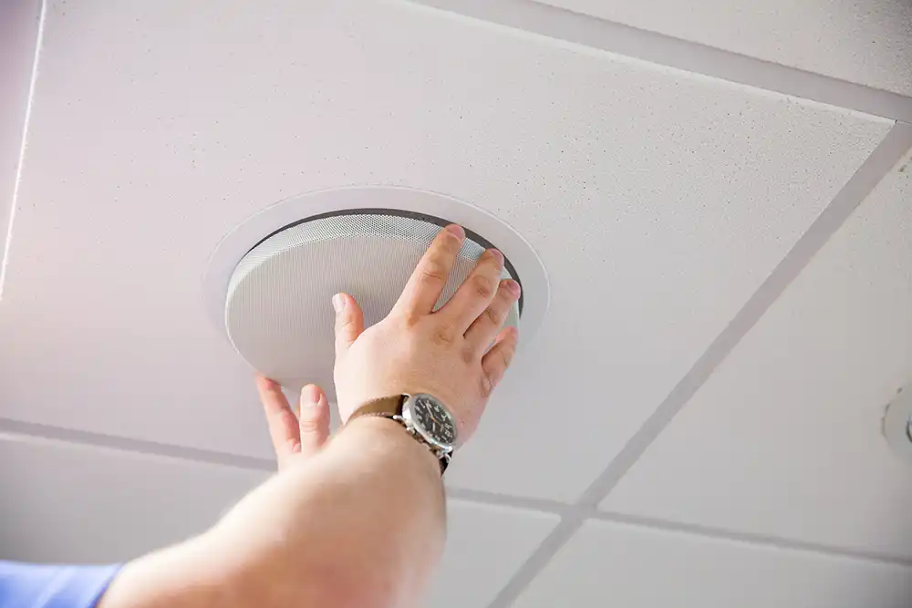 An audiovisual equipment installer is placing a ceiling speaker grill on the ceiling of a Chicago North Shore office.