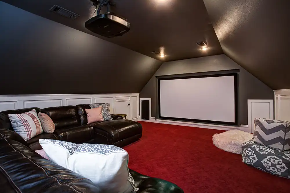 A home theater with a black leather couch and a projector screen in a finished attic of a Chicago North Shore home.