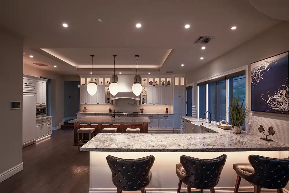 A modern kitchen with marble counter tops and bar stools and automated lighting in a Chicago North Shore home.