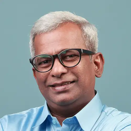 An indian man wearing glasses and a blue shirt.